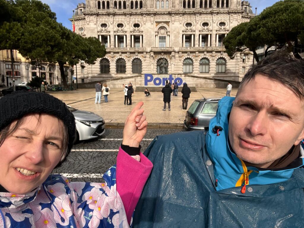 Kobieta i mężczyzna w płaszczach przeciwdeszczowych. Kobieta wskazuje na nazwę Porto.