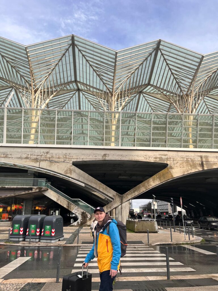 Widok na perony kolejowe w Lizbonie. Na pierwszym planie mężczyzna z walizką w niebiesko-żółtej kurtce. 